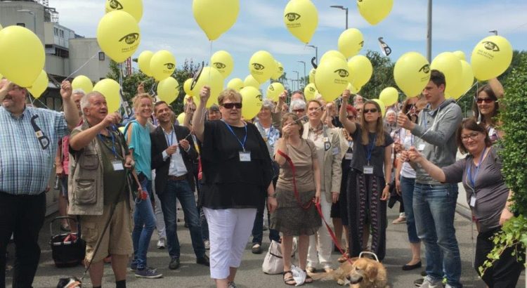 Auf dem Bild sind Menschen im freien von der Pro Retina e. V. mit Luftballons abgebildet, einige davon mit Blindenführhund.